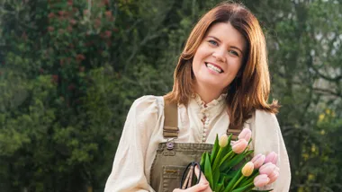 Woman holding Tulips in-front of a bush wearing overalls