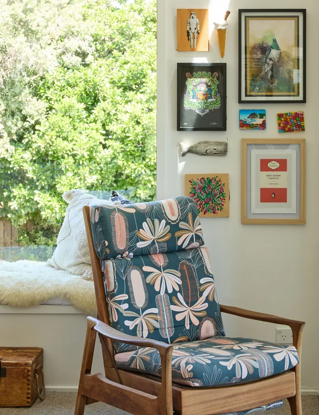 An upholstered chair sits in the corner of the living room under photo frames after the house renovation in Christchurch