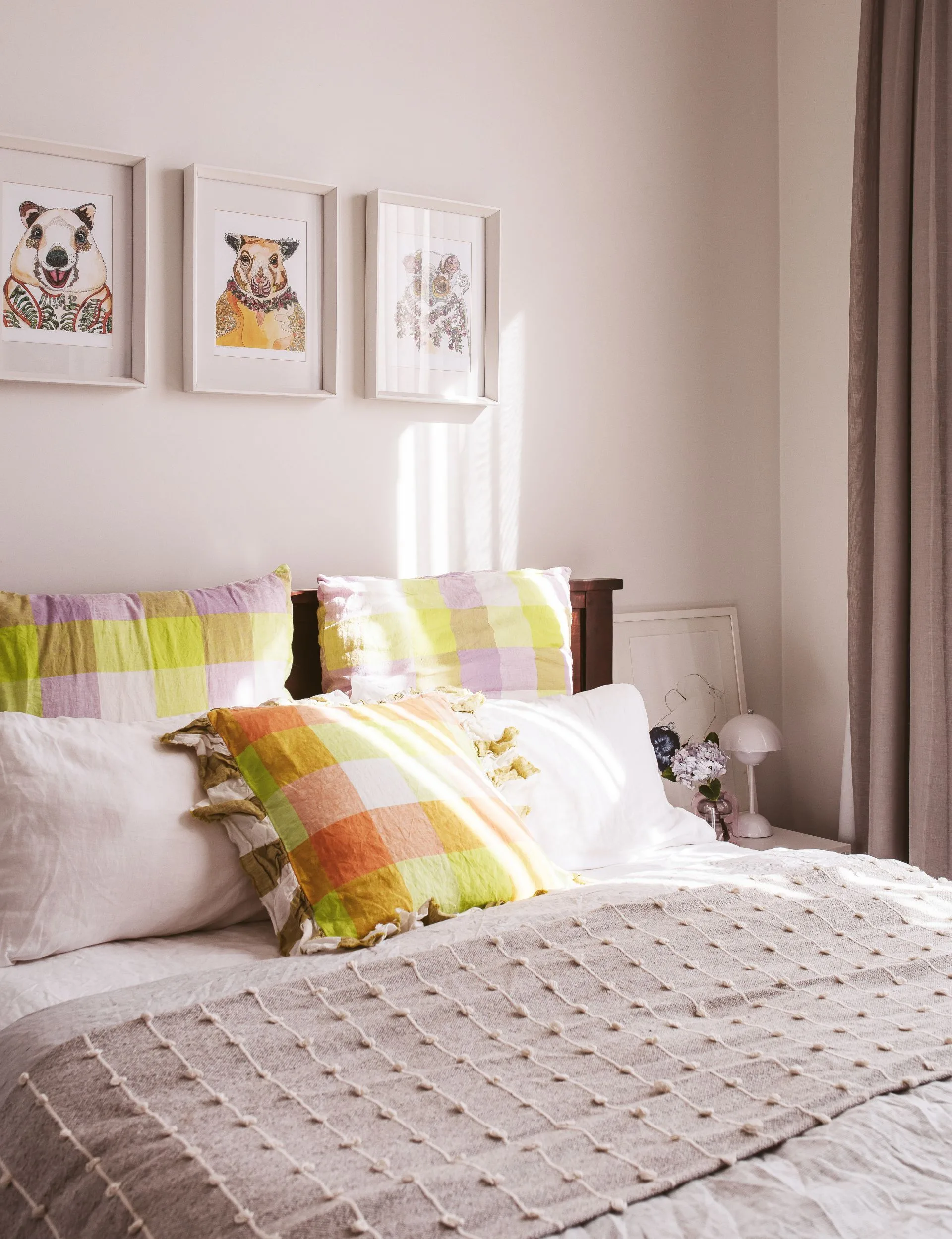 The renovated New Plymouth villa guest bedroom has white walls with three small framed painting of animals above the bed