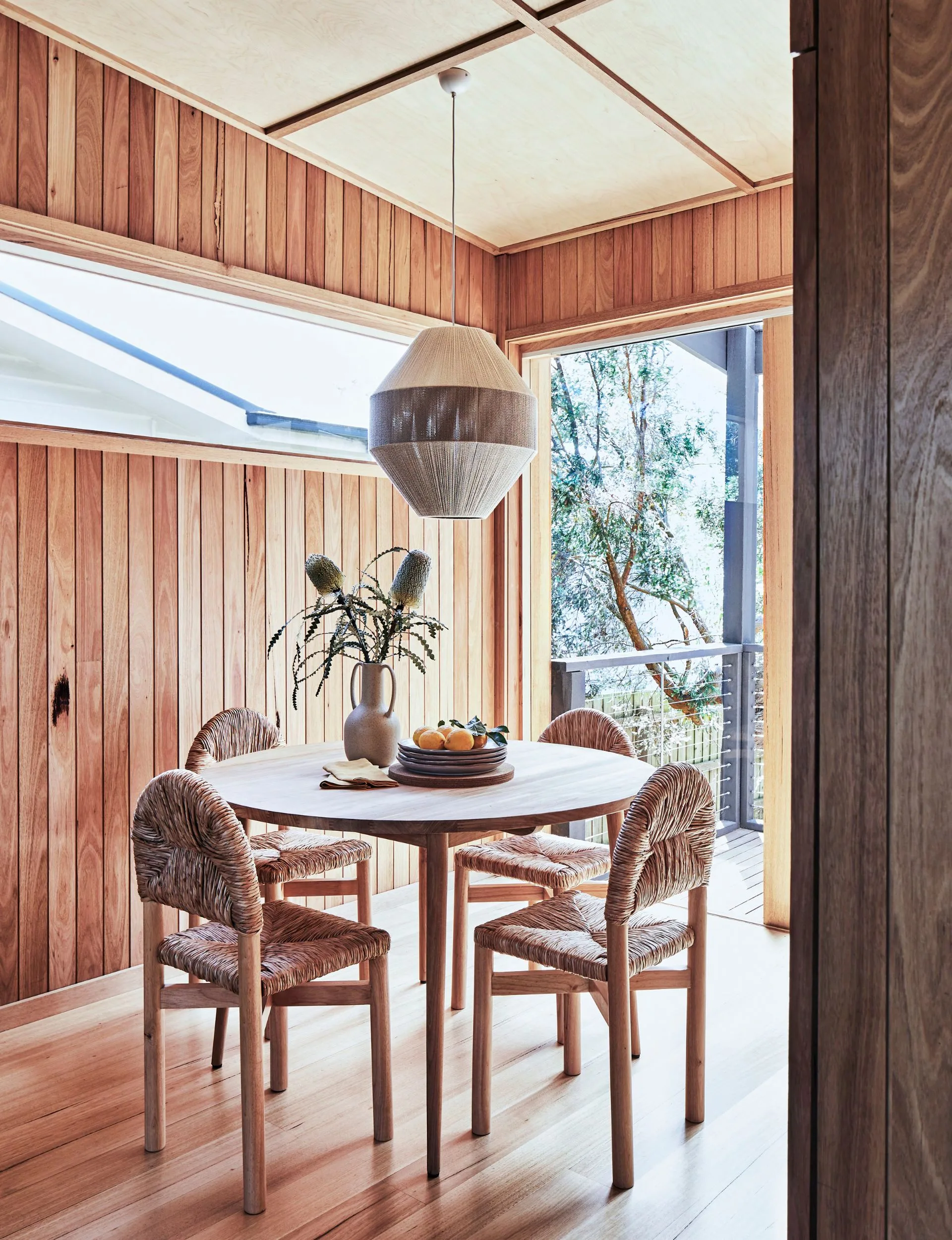 The round dining room table with a round pendant light hanging overhead in the renovated beach cabin