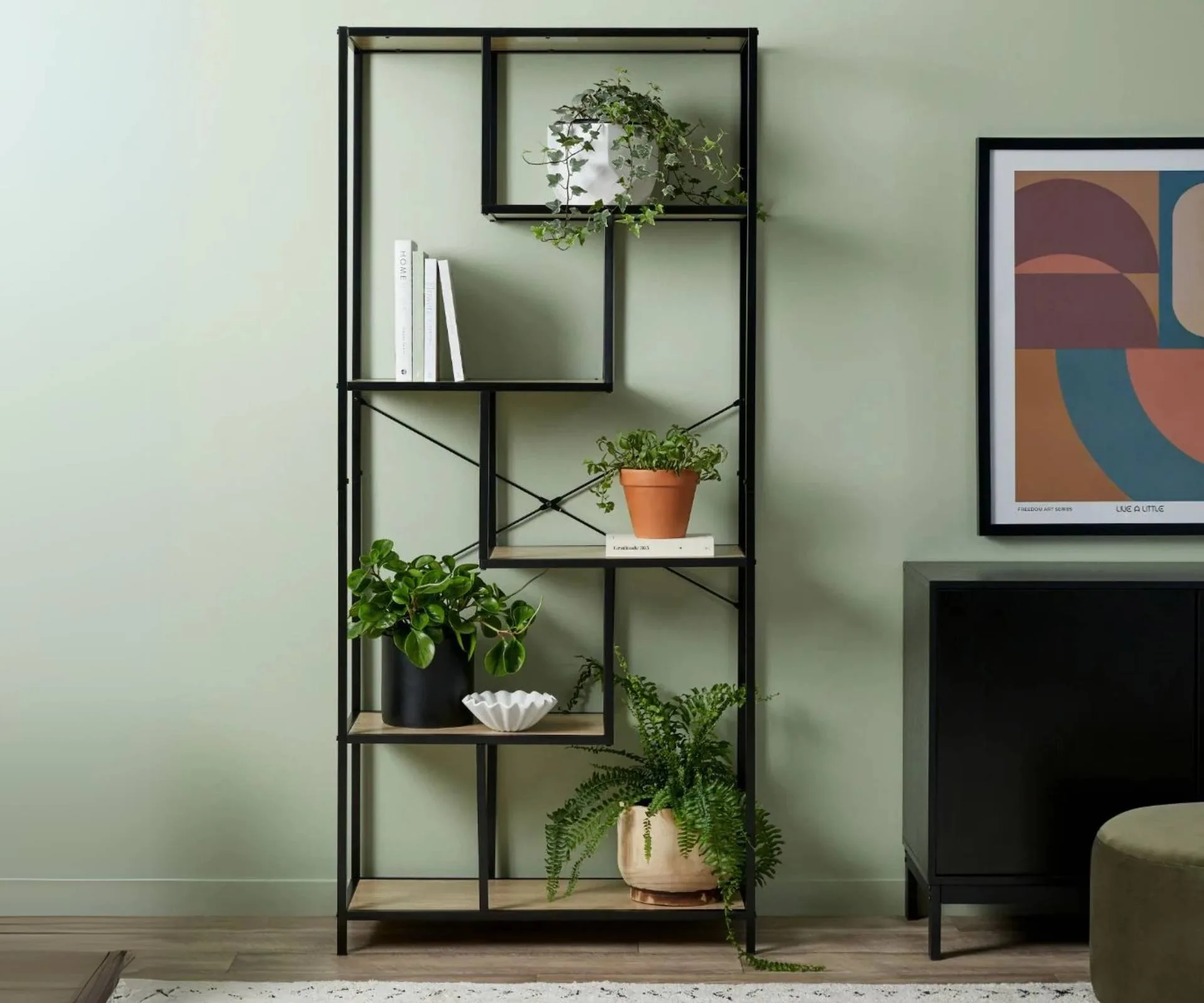 A black plant stand against a green wall, with four plants sitting on the stand. 