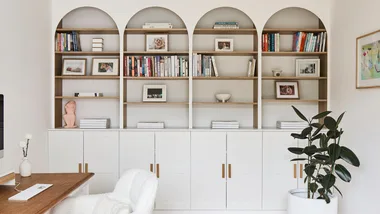 A white painted bookcase filled with books and a green plant and desk.