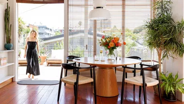 The inside of a white villa with a woman wearing a black dress walking into a dining room.