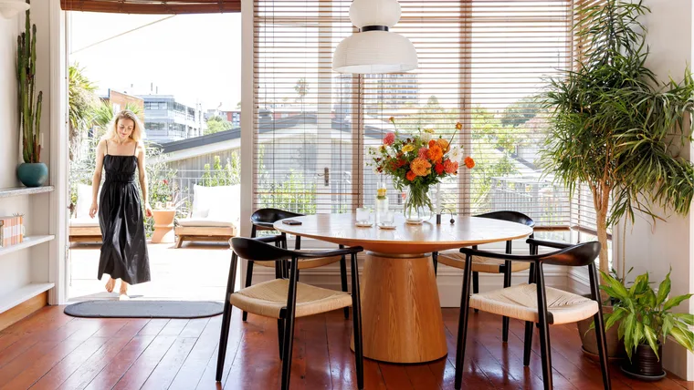 The inside of a white villa with a woman wearing a black dress walking into a dining room.