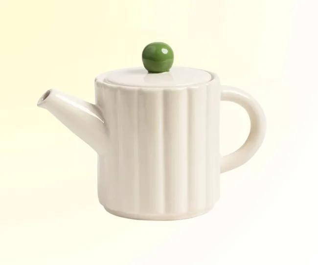 A white teapot with a green top against a yellow background