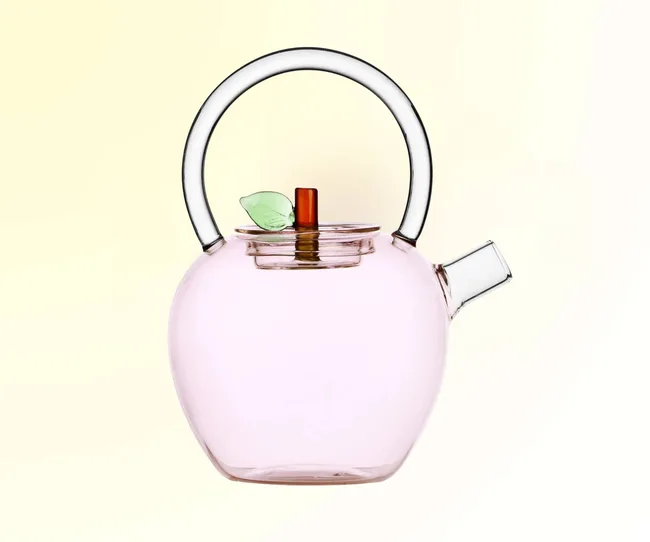 A pink glass teapot against a yellow background