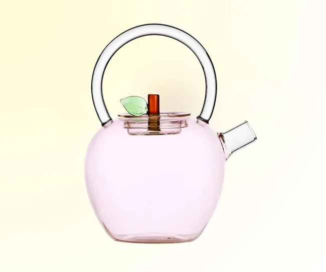A pink glass teapot against a yellow background