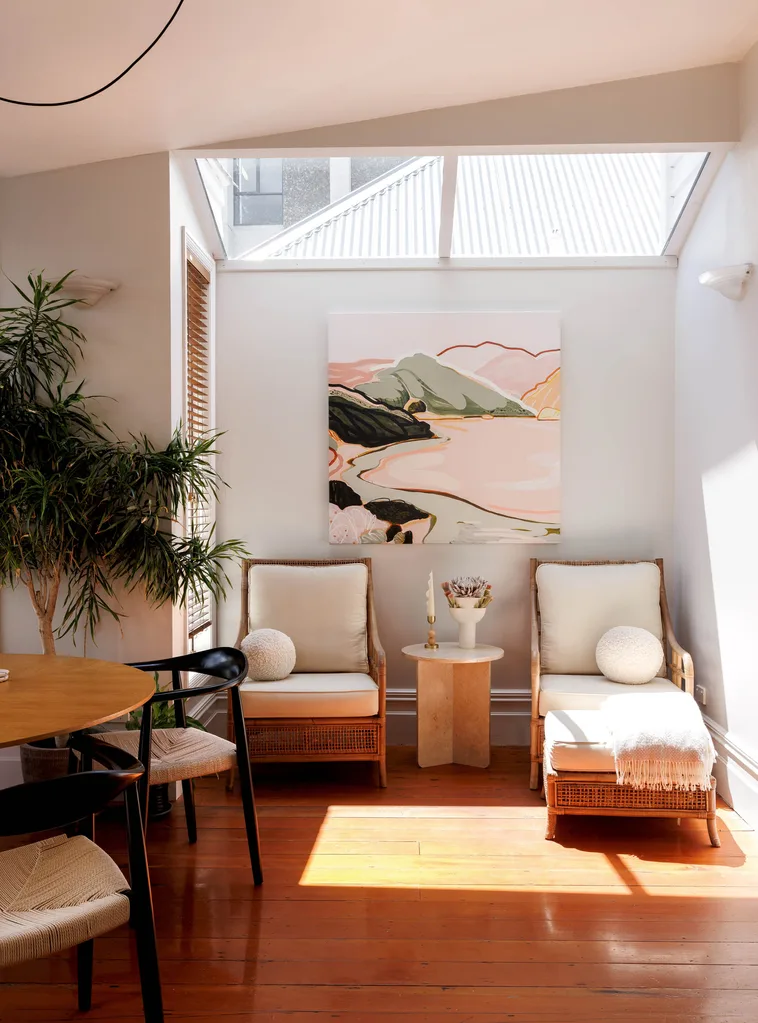Looking into a sitting area with two cane armchairs, a skylight and an abstract landscape painting hanging on the wall.