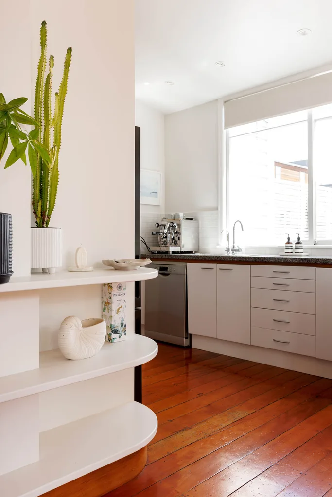 Looking into a kitchen with wooden floors and windows above the bench and sink.
