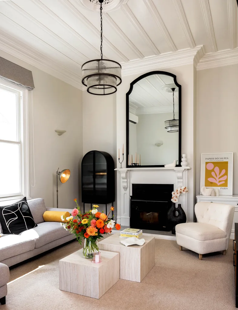 The sitting room of a white villa with a mirror above a fireplace and white sofas surrounding two square coffee tables.