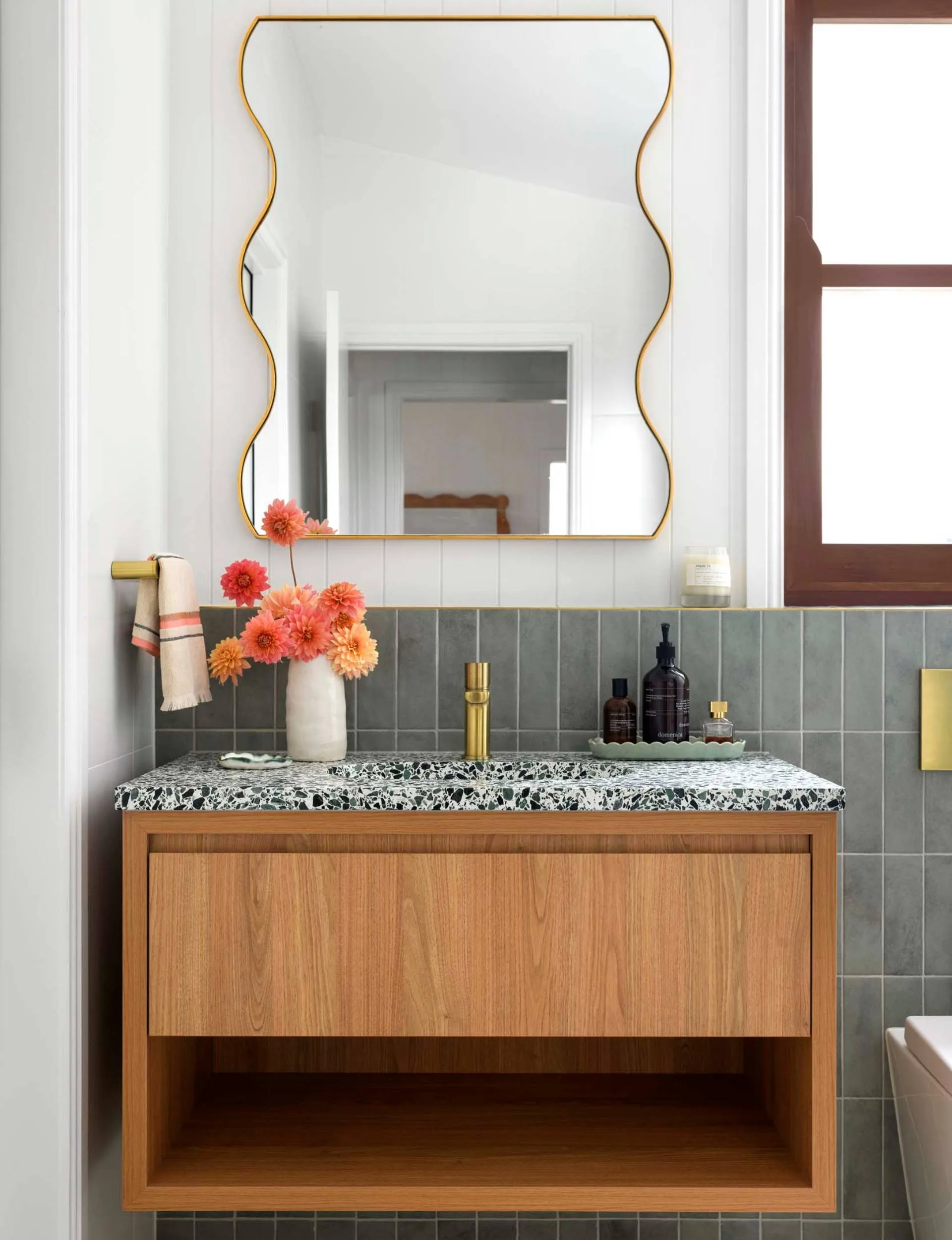 Deep olive tiles line the bottom half of the bathroom, with white on the top half and a wavy mirror in the middle
