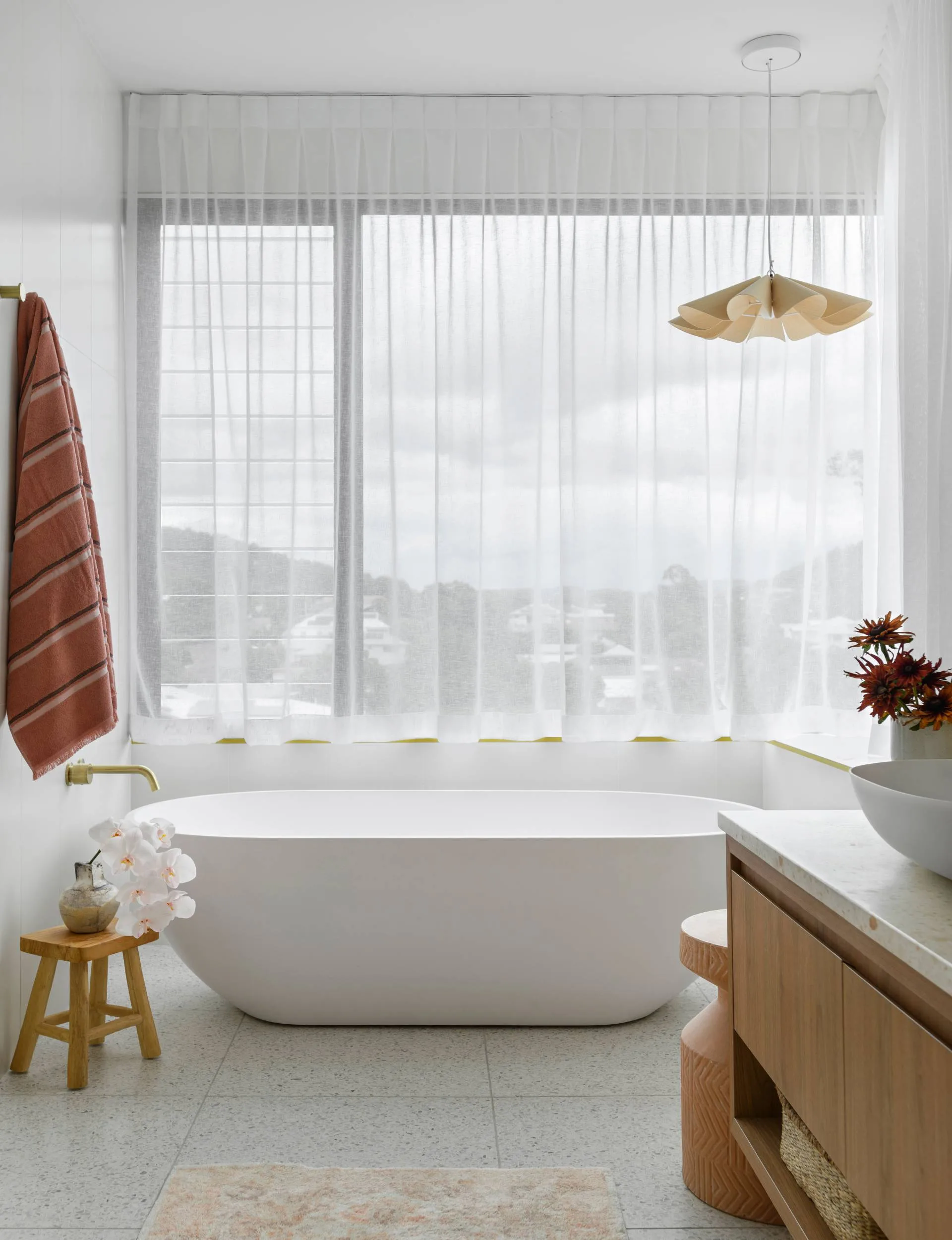 A free-standing oval white bathtub under a window with flowy white curtains