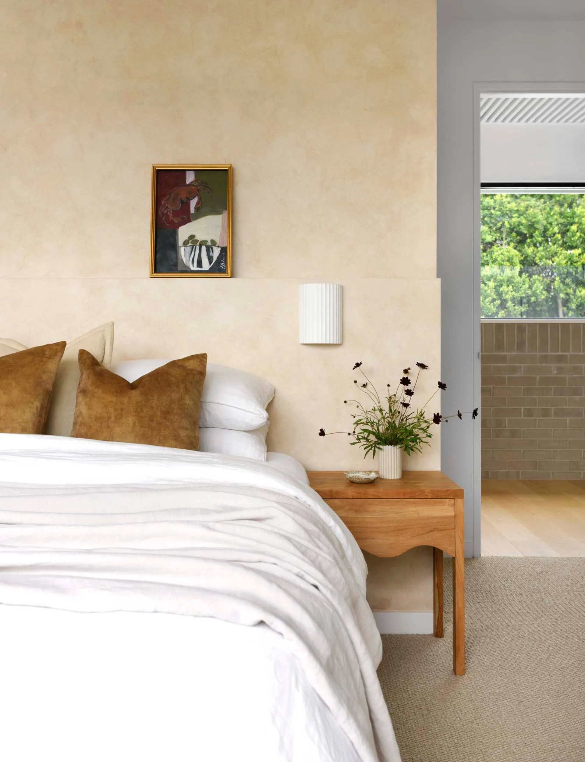 White bedding and yellow cushions on a bed against a beige painted mid-century-inspired bedroom