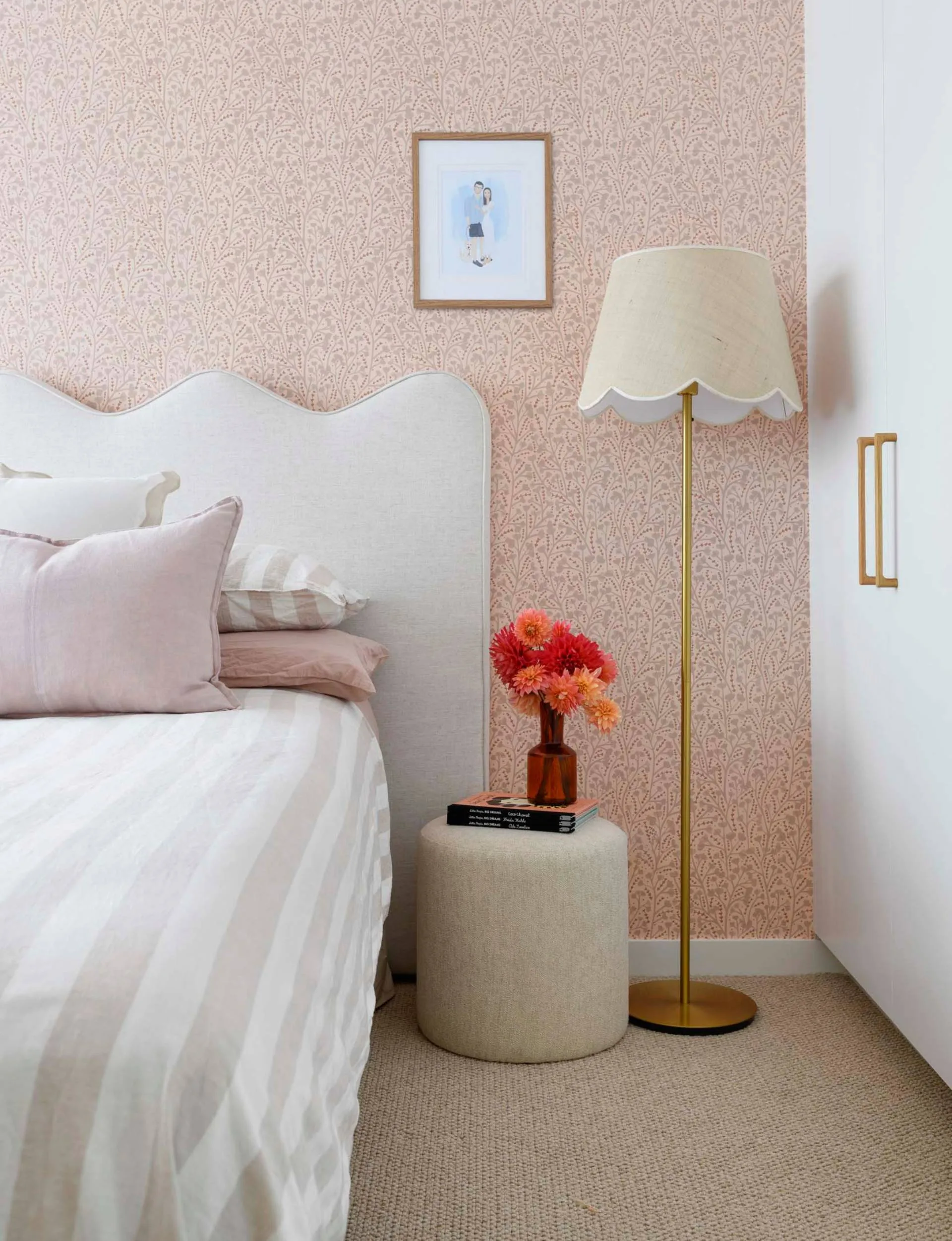 A white bed with a wavy headboard against a pink floral wallpaper