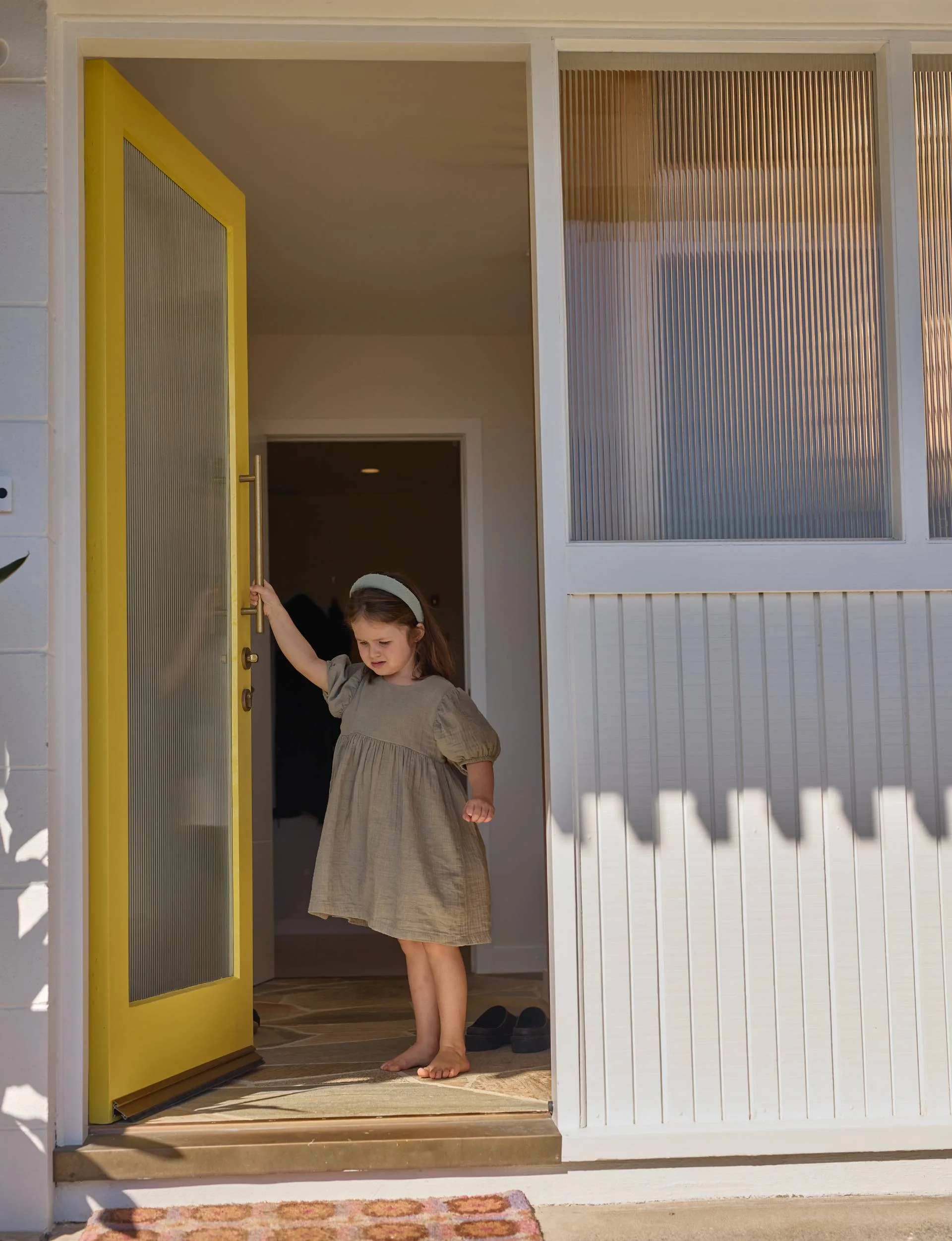 Toddler Maisie opening the yellow front door of the 70s home