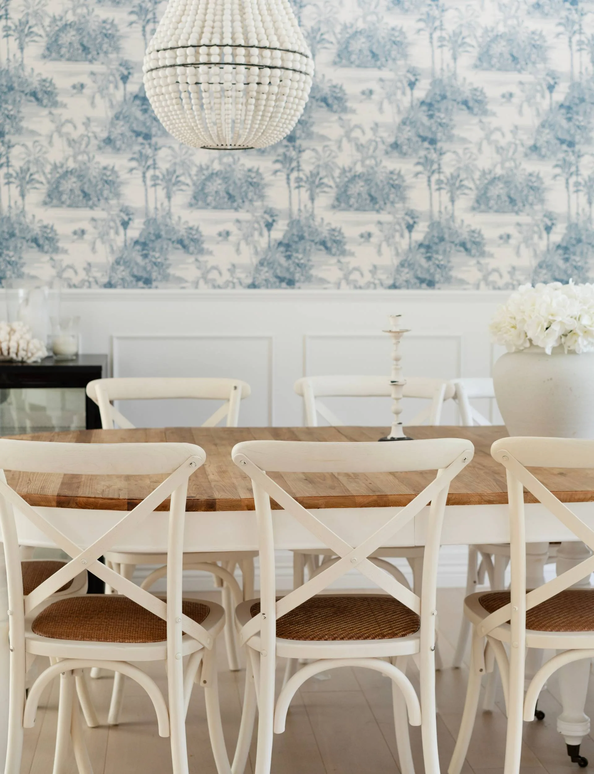 An oval dining room table with white and blue wallpaper around the walls