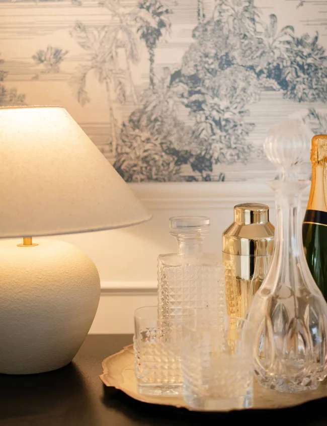 Glasses ang a whine bottle on a tray on a side desk beside a white lamp