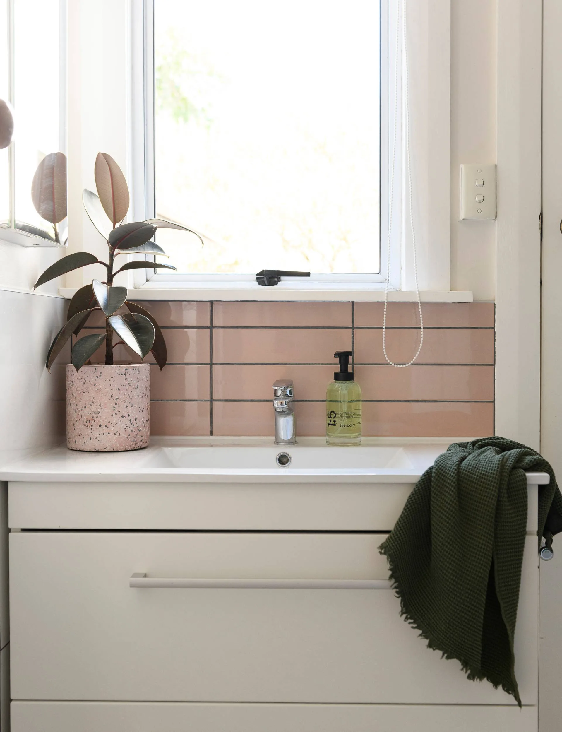 A bathroom with light pink tiles above the sink