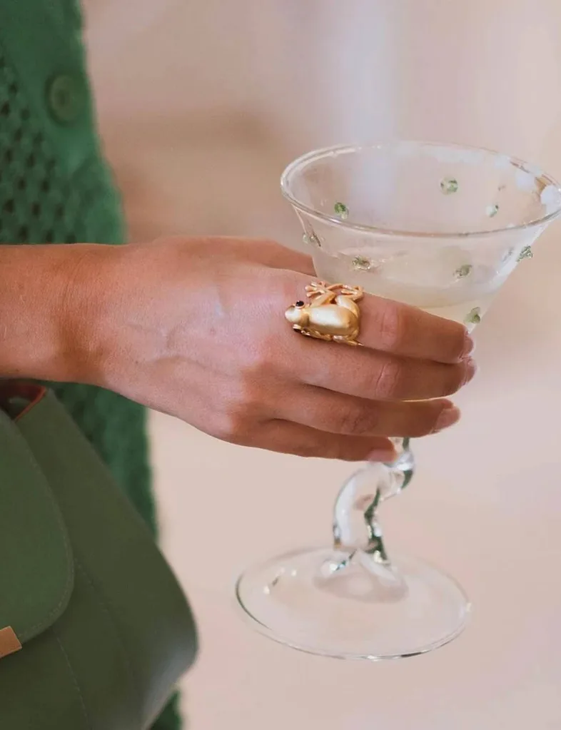 A spiked wine glass held by a woman wearing a frog ring.