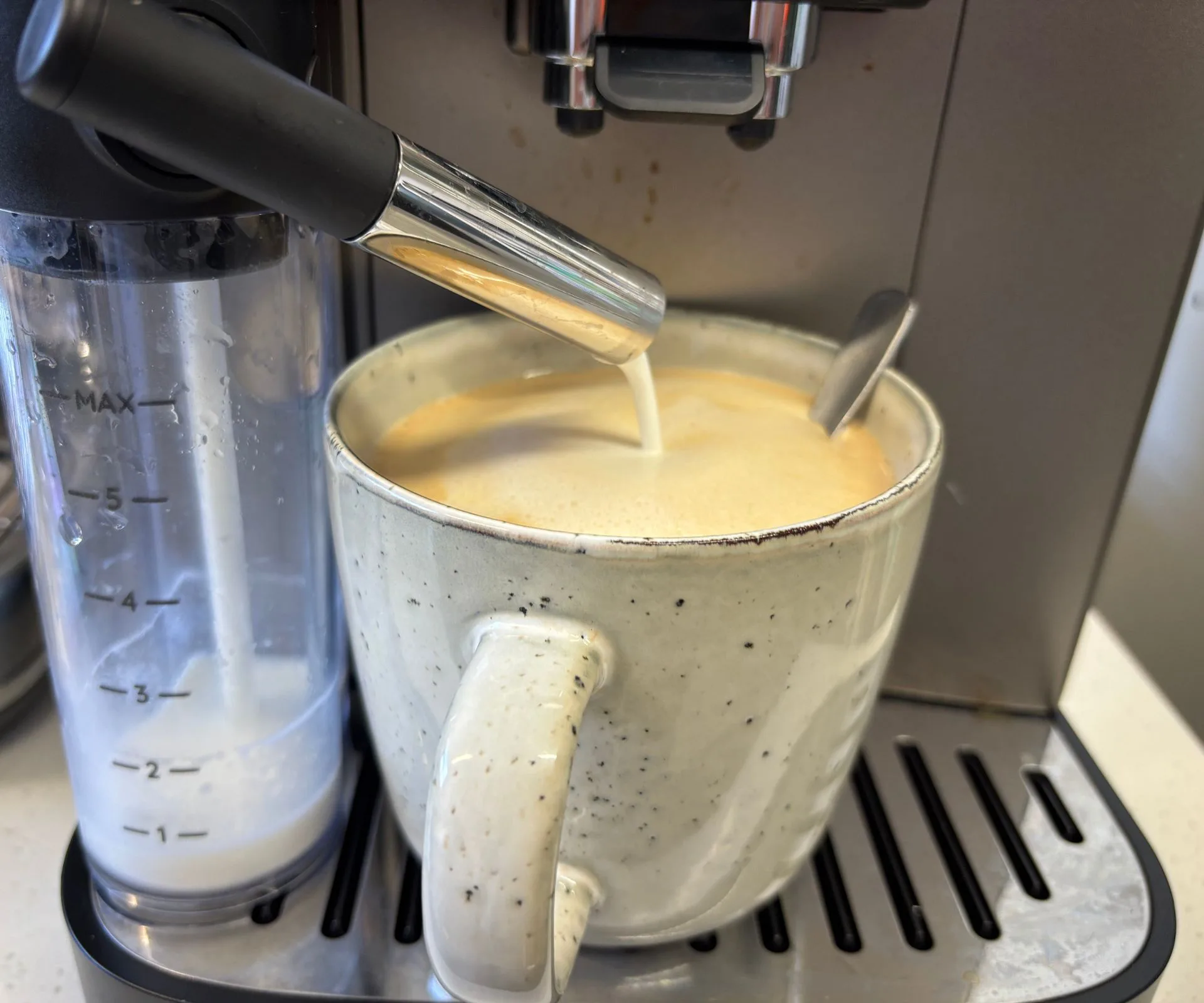 a large frothy coffee in a china mug being made using the coffee machine