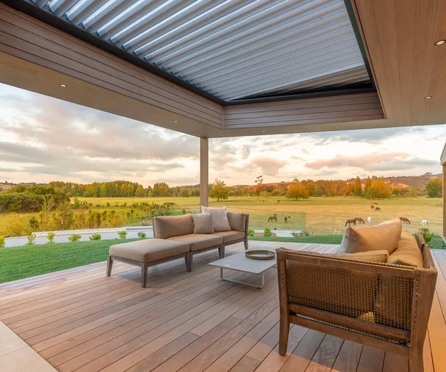 A covered deck with sofas and a coffee table overlooking a field full of horses.