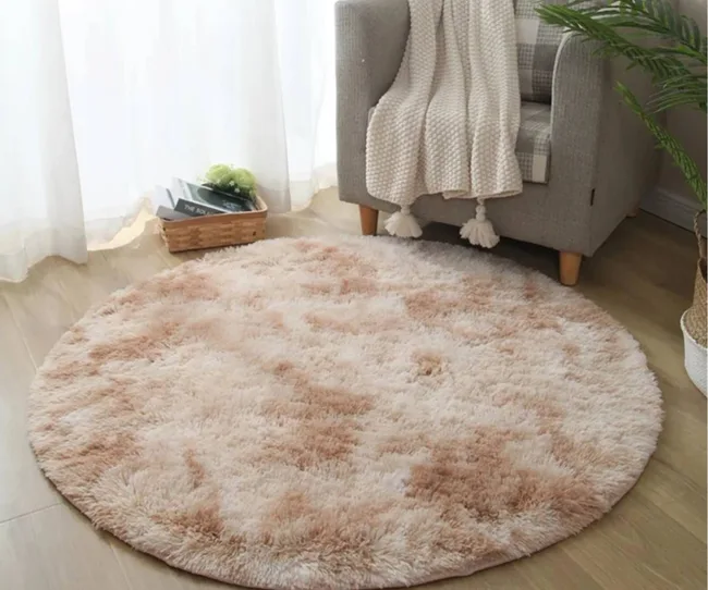A nude coloured round rug with an occasional chair.