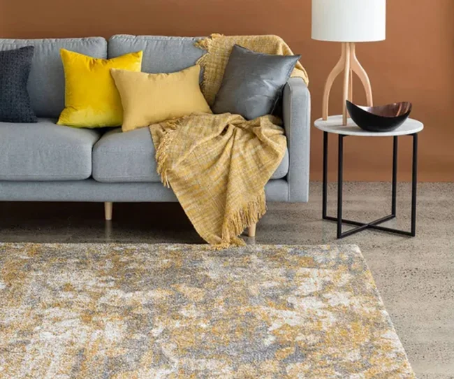 A patterned yellow rug with a sofa and side table.