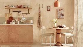 A limewashed kitchen with a small round dining table and two white dining chairs, as well as a bench with appliances on top.