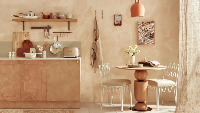 A limewashed kitchen with a small round dining table and two white dining chairs, as well as a bench with appliances on top.