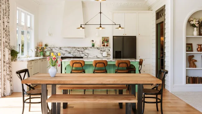 A kitchen with a green island, dining table and chairs, and a chandelier