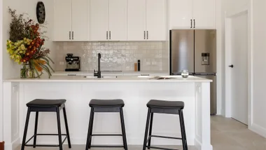 Liam Messam's kitchen with white cabinetry and island, Haier appliances and black bar stools