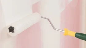 Paint roller with white paint being using on a wall