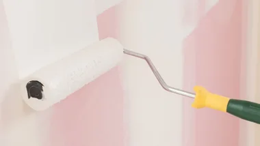 Paint roller with white paint being using on a wall