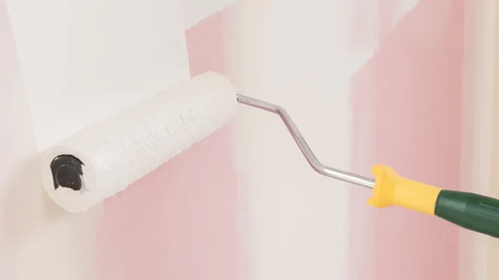 Paint roller with white paint being using on a wall