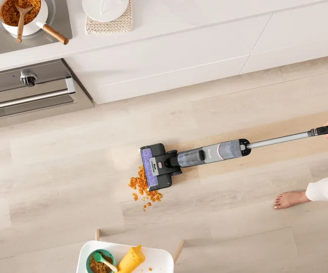 Lady using the Shark HydroVac to clean up pasta on wooden floor