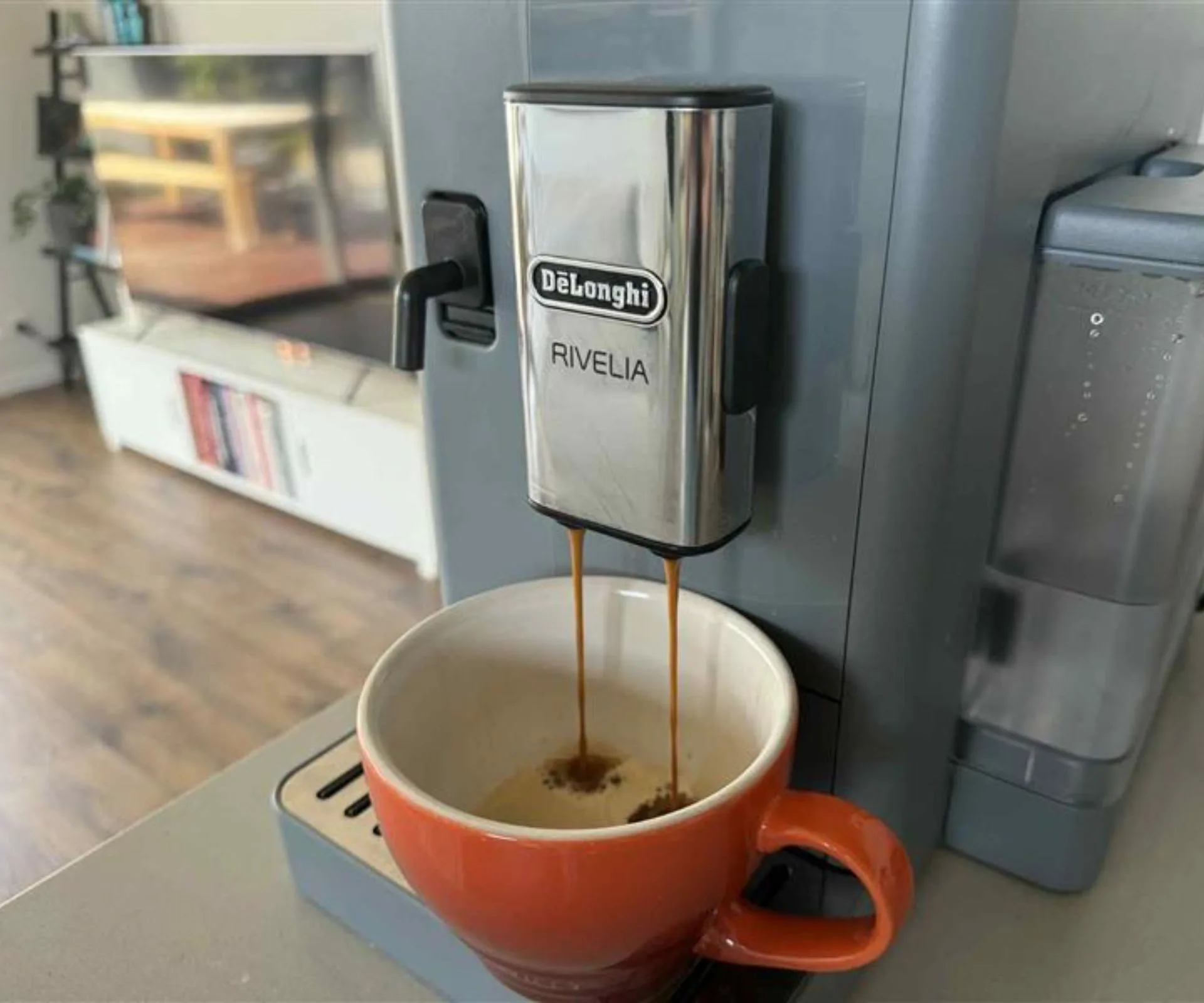The De&rsquo;Longhi Rivelia pouring coffee into an orange mug 