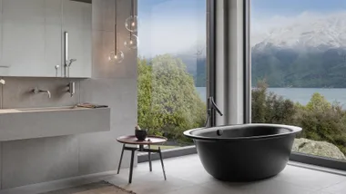 A black freestanding bath, with floor to ceiling windows looking out to a lake.