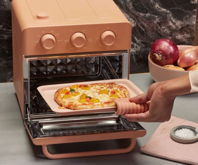 A peach wonder oven with a pizza coming out of it
