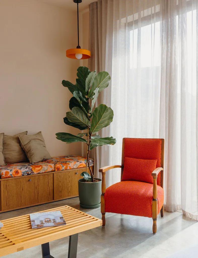 The soft pink wall is contrasted by bright coloured decor like this orange chair in the living room