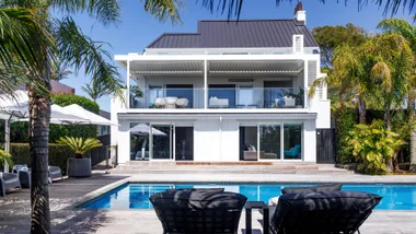 The exterior of a white pool, with a lap pool in foreground and tropical trees