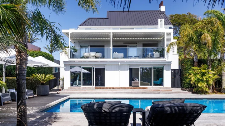 The exterior of a white pool, with a lap pool in foreground and tropical trees