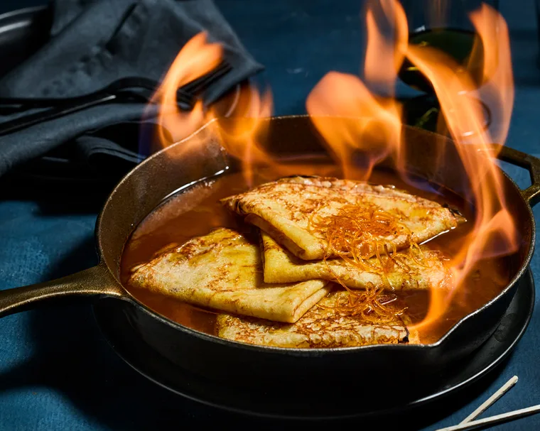 cr&ecirc;pes Suzette in a cast iron pan with candied orange peel and sauce with flames