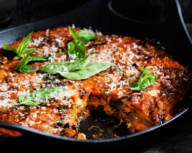 Eggplant parmigiana with basil and parmesan on top, served in a black serving dish