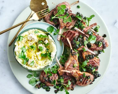 Lamb cutlets with feta skordalia and micro herbs on white plate with gold spoon and fork.