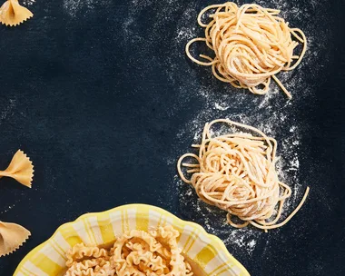 Types of pasta shapes, showcasing uncooked tagliolini, agnolotti del plin and farfalle pasta types on a dark coloured background