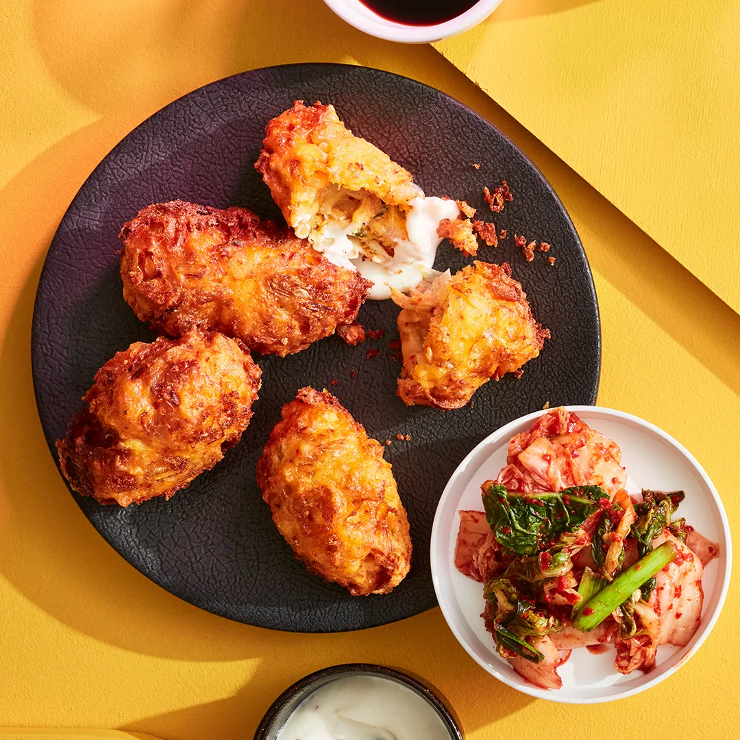 Korean kimchi fritters on black plate with bowl of kimchi to side on yellow background.
