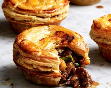 Beef rendang mini meat pie with flaky folden pastry and filling spilling out of biten pastry