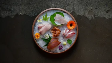 A plate of sashimi garnished with flowers on black background.