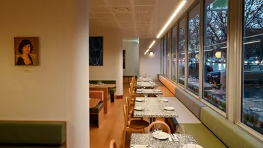 A view of the dining room at Sofia, with a banquette on the right-hand side and a portrait on the wall.