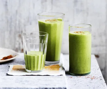 Three tall glasses holding a light-green smoothie, garnished with a sprinkle of cinnamon.